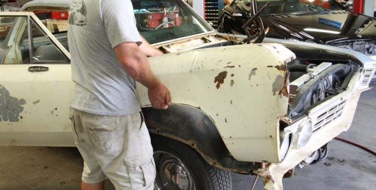 A restoration shop working in shorts and gray shirt removing a right-side fender from an El Camino showing the work at restoration shop risk
