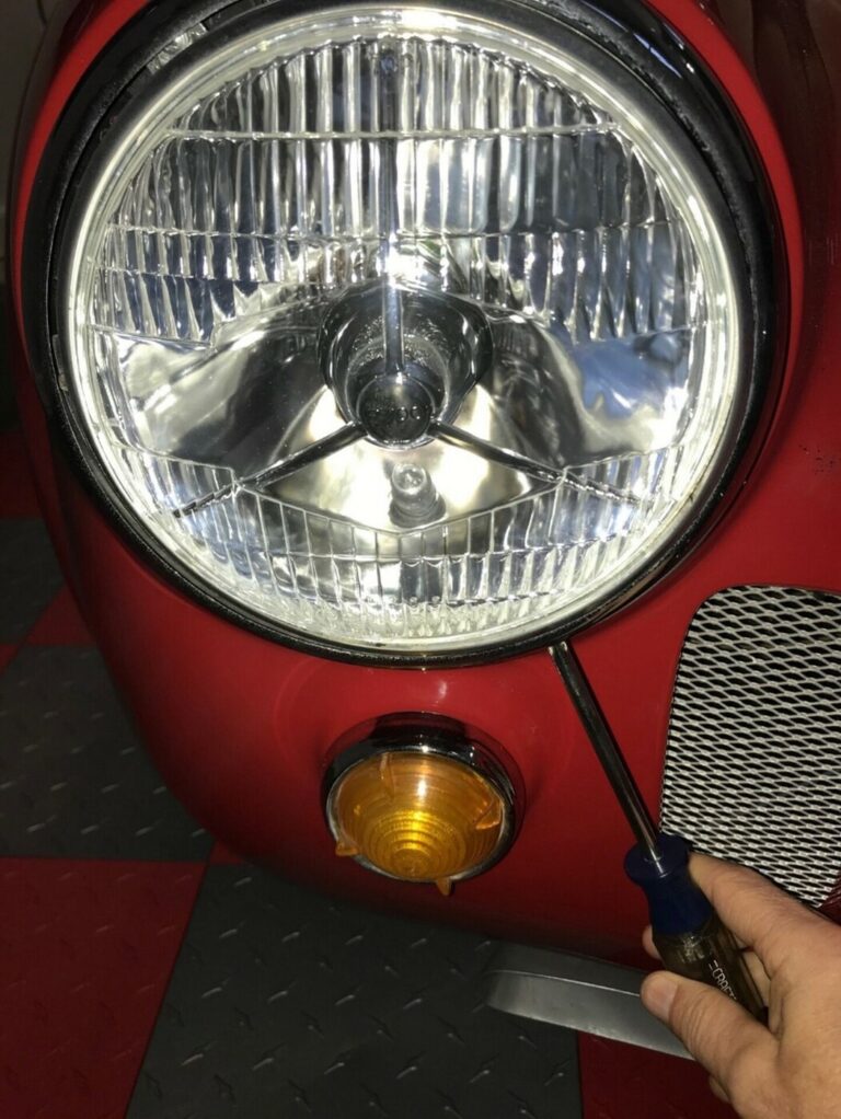 A mechanic working on the right-side headlight of a Cobra during the car restoration guidelines process