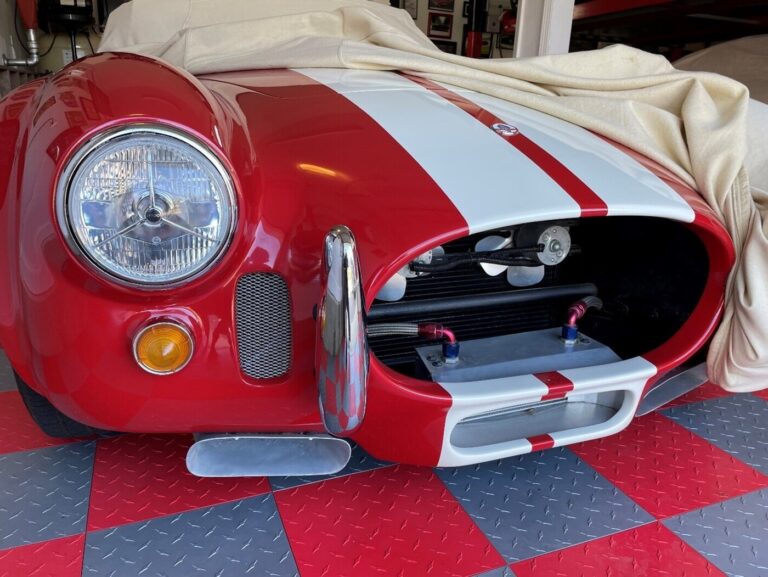 Front of a red and white Cobra with a car cover partially removed at home from the repair shop after using car restoration guidelines