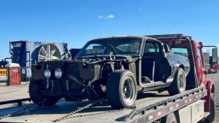 Black Ford Mustang GT500 on a red flatbed truck driving on a highway head for repairs noting the car restoration risks