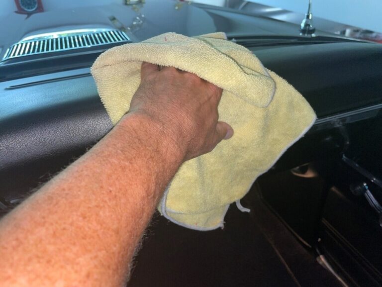 A man wiping down the dashboard of a Chevelle with a yellow towel to clean up the car to avoid common mistakes when selling a classic car