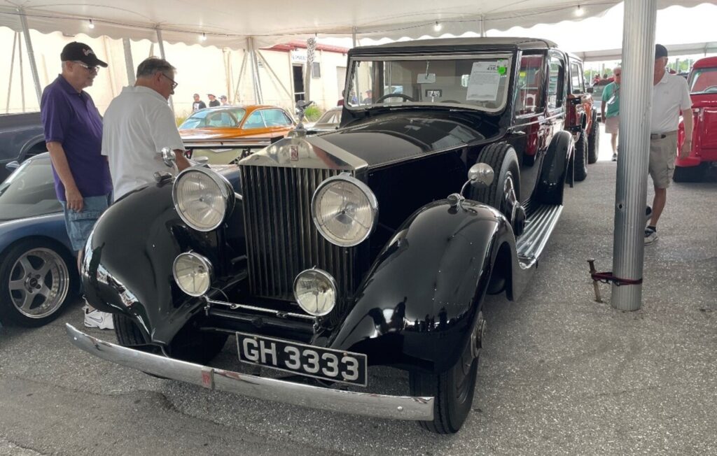 A black vintage Rolls Royce under a tent at a classic car auction with people inspecting the car for classic car investing