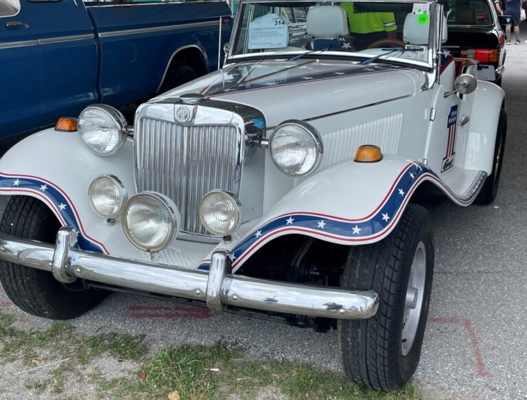 A custom painted white MG convertible with red, white, and blue stripes and stars with a number 1 painted on the side for sale as classic car investing