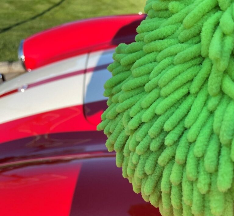 A green car washing Mit to be used in classic car washing in front of a red with white stripes Cobra