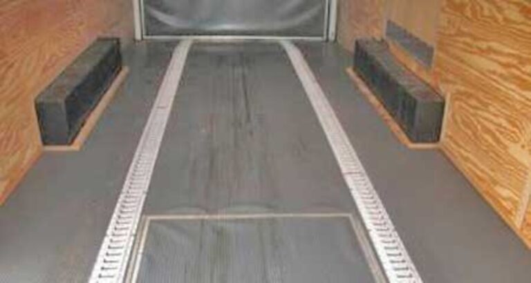 The inside of an enclosed car trailer with wood walls, finished floor with track tie down system and noting the low height of the inner fender wells