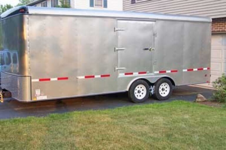A silver with red/white reflective tape on the side with white wheel car trailer parked in a driveway