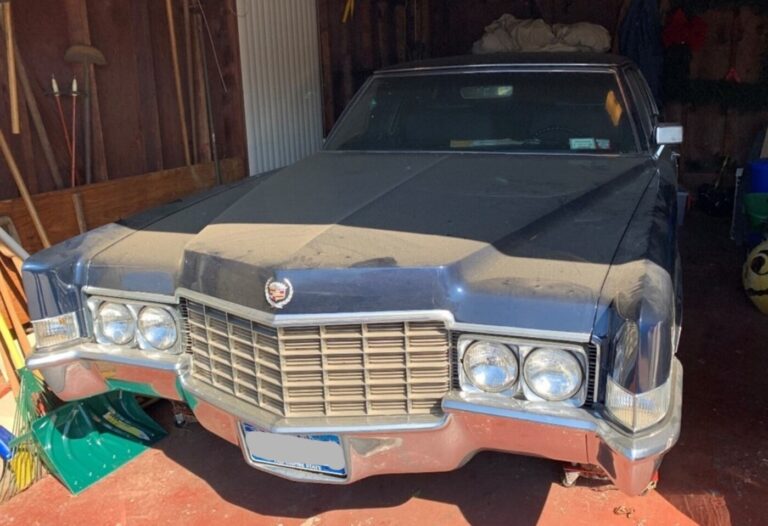 A blue Cadillac with dust on its hood parked in a garage needing car storage preparation