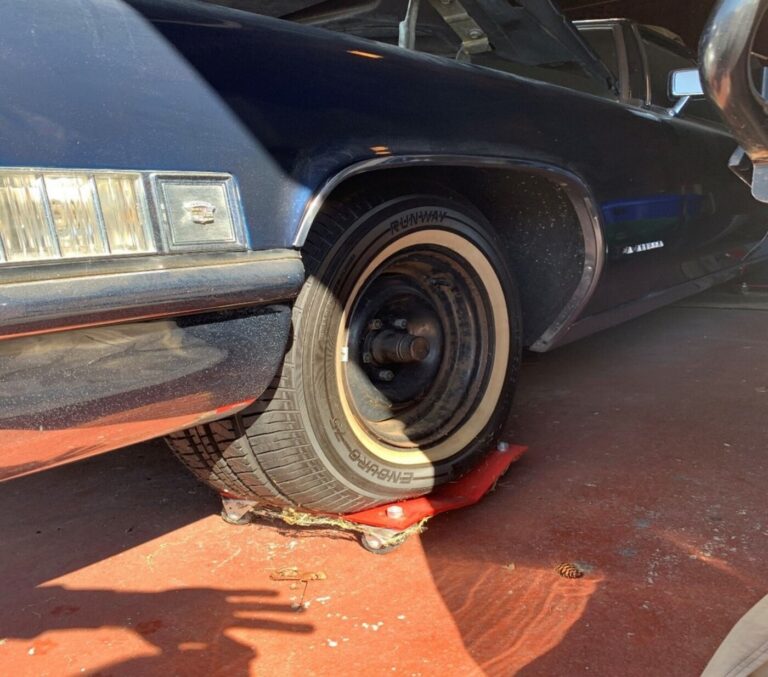 A blue Cadillac front left flat tire on a wheel dolly as part of car storage preparation