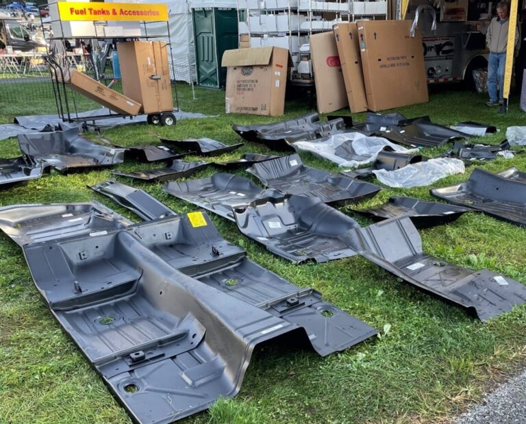 Metal car floor plans for GM cars as well as other aftermarket car parts laying on the grass at a flea market