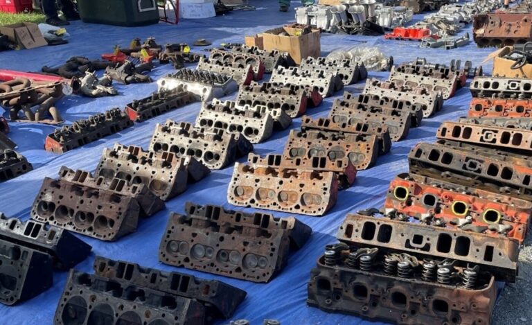 A variety of V8 engine heads and other engine car parts for sale displayed on a blue tarp