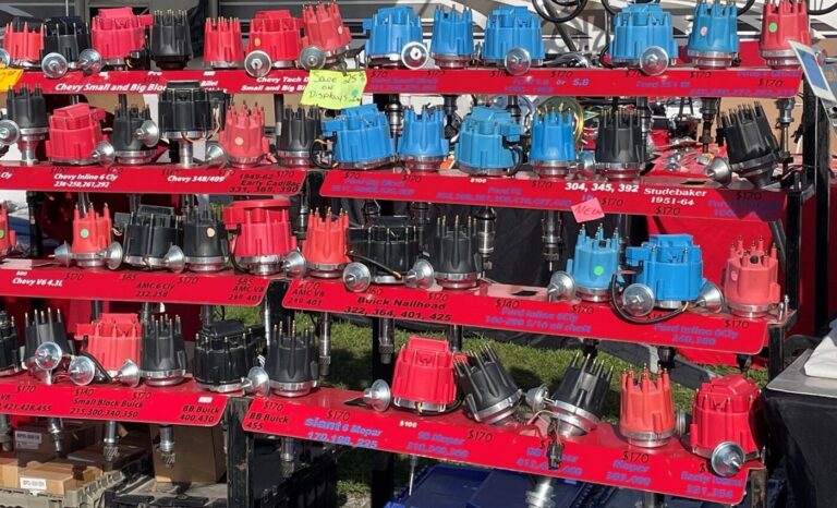A variety of car engine distributors in blue, black, and red caps for sale at a flea market