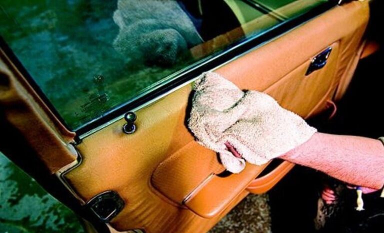 A person cleaning the tan interior of a vintage car with a white cloth preparing for the car sales
