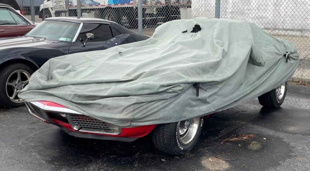 A red C3 Corvette under a cover in a parking lot next to an 80 Corvette waiting on repairs; steps to avoid car restoration shop scammers for car success