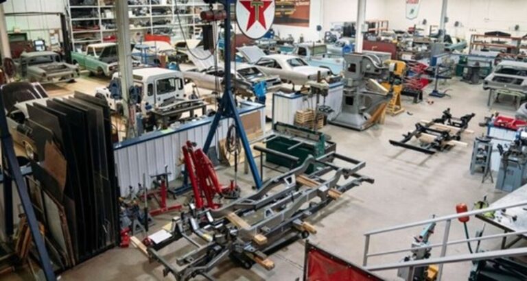 Looking down inside a classic car restoration shop with various work stations and project cars and frames; making sure you research companies to avoid car restoration shop scammers