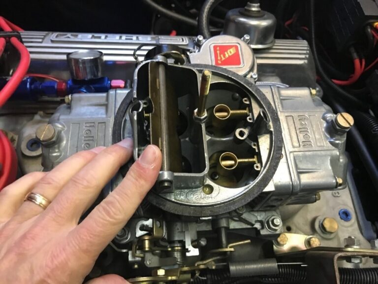 A mechanic inspecting a silver 4-barrel Holley carb as part of regularly scheduled car engine maintenance