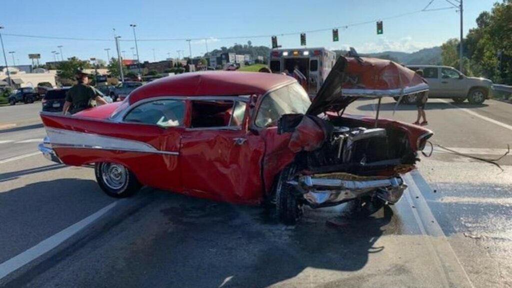 A red 57 Chevy Belair sitting in the middle of the road with front end damage requiring vintage car insurance