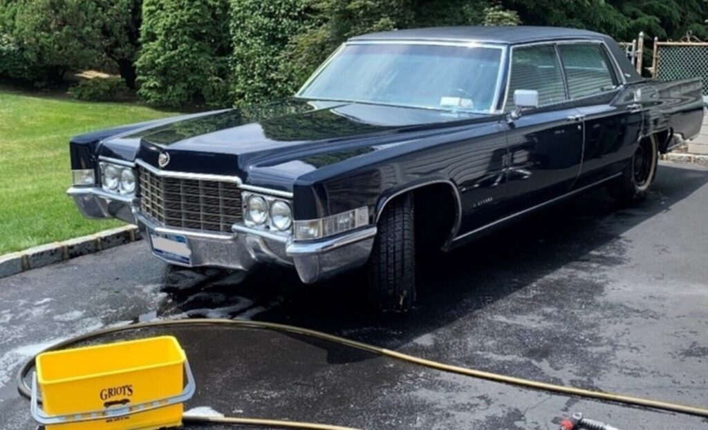 A black 4 door Cadillac in a driveway with a hose and water bucket being cleaned and avoiding car washing mistakes