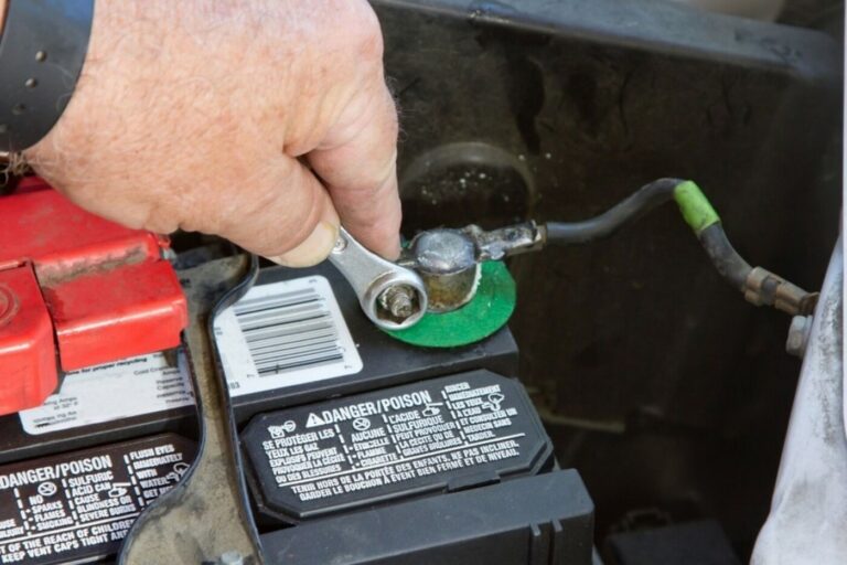 A person with a wrench removing the bolt holding the wire to the car battery to remove the connection as part of the car winter storage