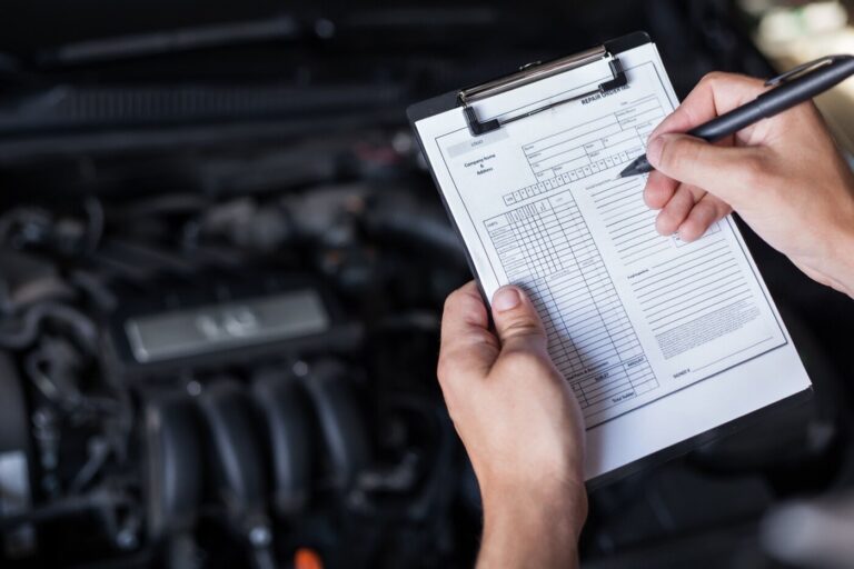 A mechanic using a checklist to inspect a vintage car for common noises classic cars make