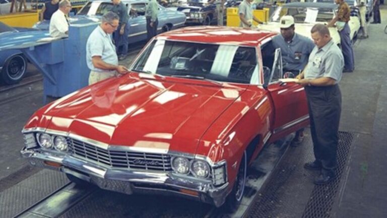 A red 60s Chevrolet on a factory assembly line being inspected by 3 workers for common noises