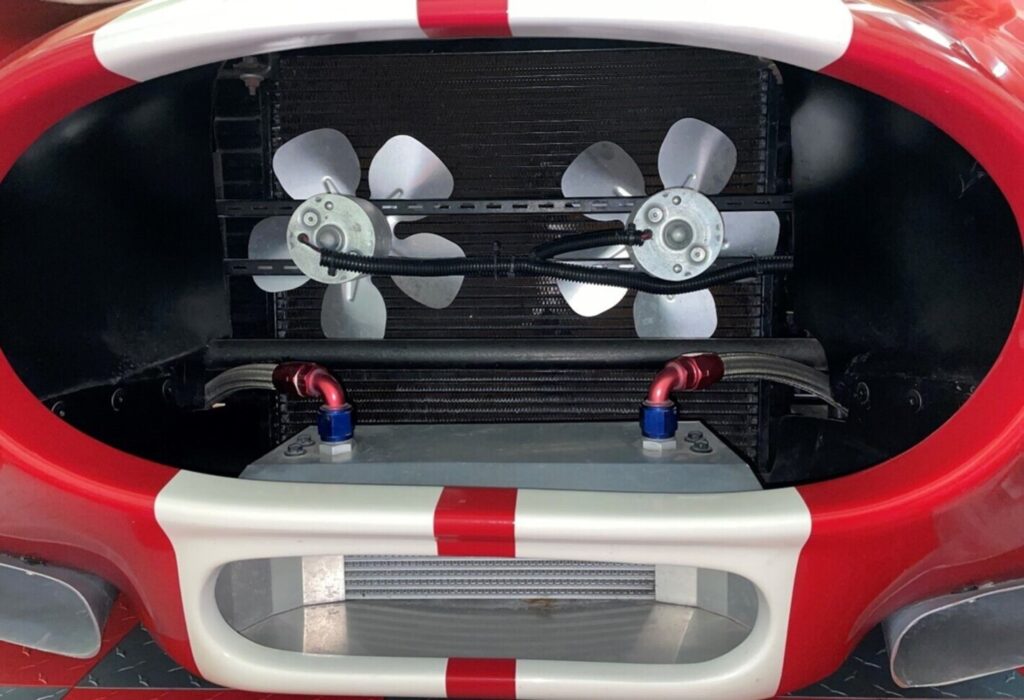 The front of a 1965 red and white Cobra whowing dual fans, oil cooler and air vents for various car engine cooling methods