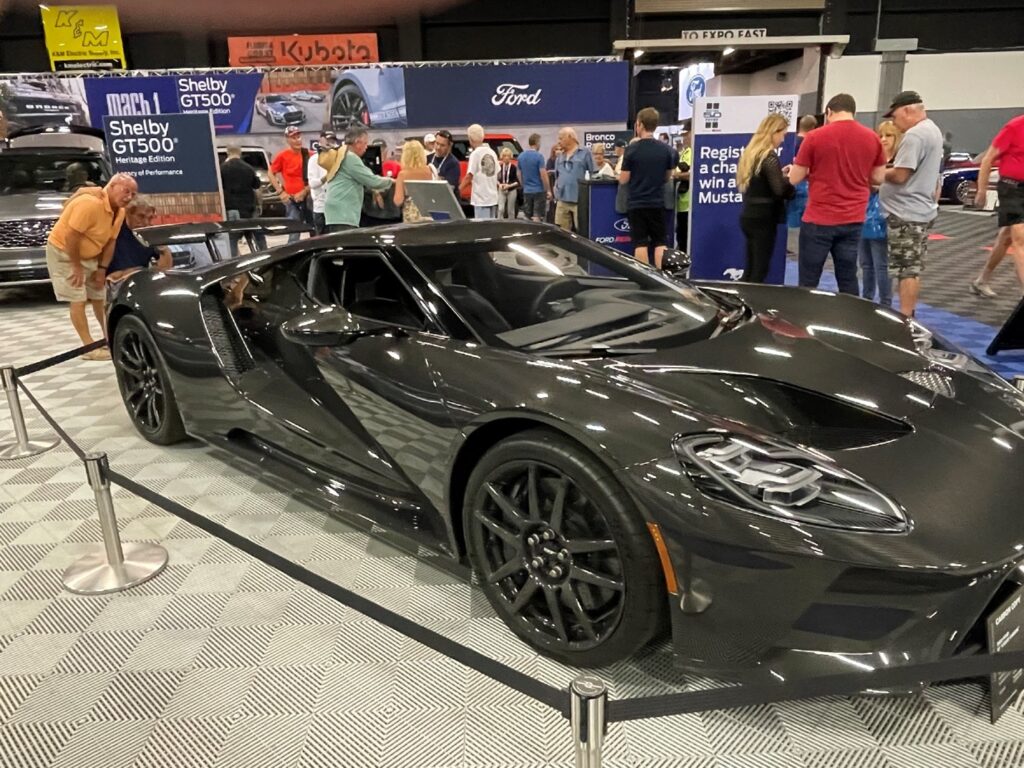 A gray Ford GT on display at a car event in a Ford display with potential buyers looking for car collections or investments