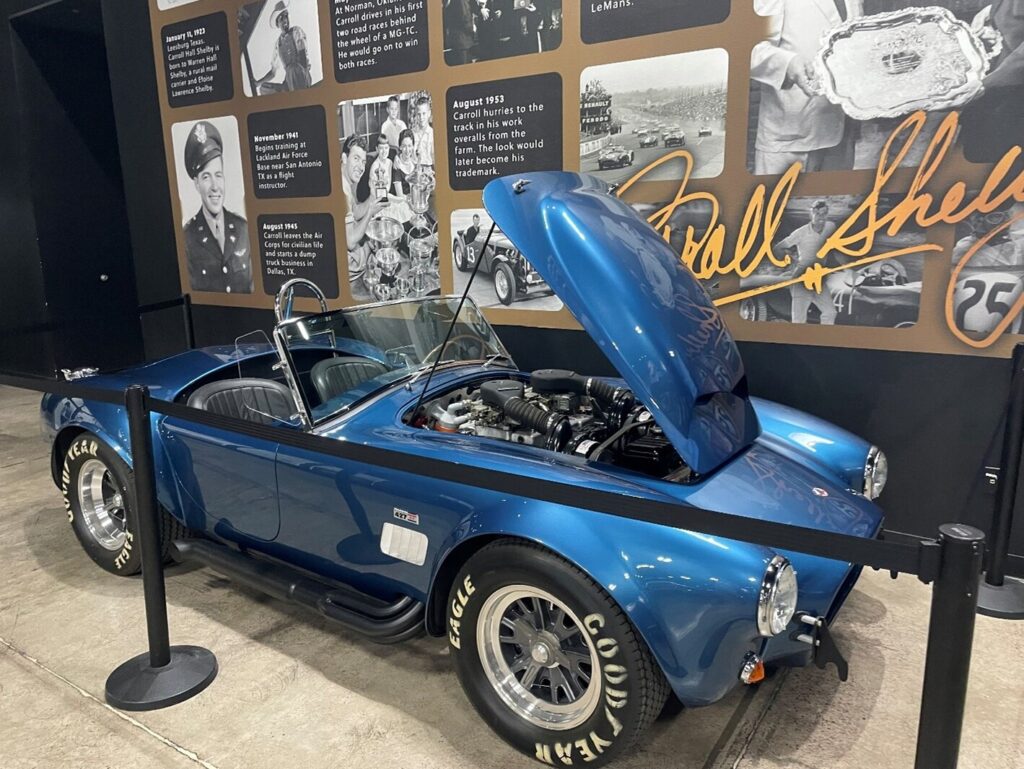 The blue Super-snake Shelby Cobra at the Shelby museum with a history timeline on the wall behind the car showing classic car provenance