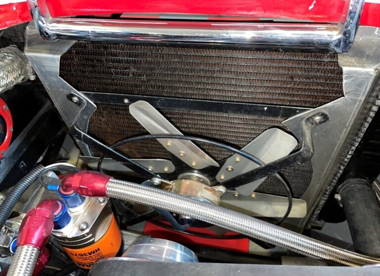 Inside the engine compartment of a red Cobra showing an electric cooling fan, and remote oil filter and lines showing car engine cooling methods