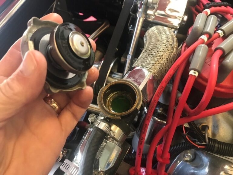A personn holding the radiator cap over the fill opening full of engine coolant next to the distributer with red wires on a Ford engine