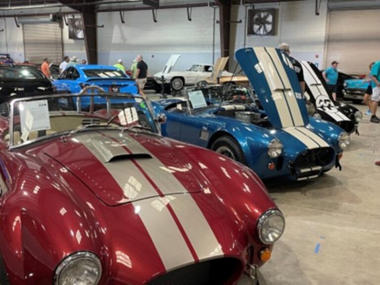 A row of red, blue and black Cobras for sale at a car auction with people looking for classic car collections