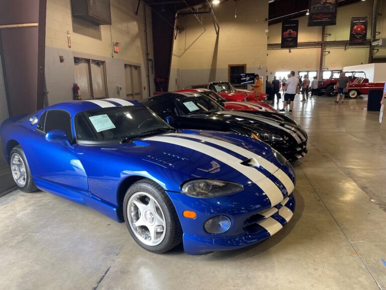 A row of blue, black, and red Dodge Vipers for sale at auction with people looking for classic car collections
