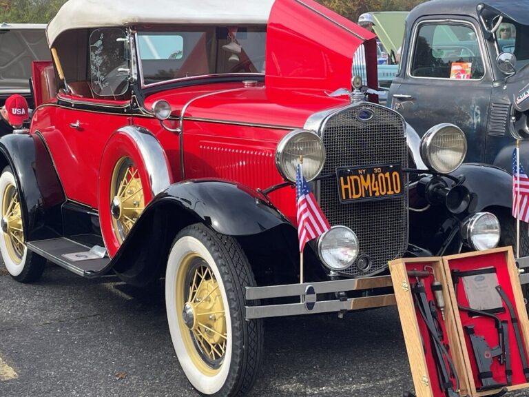 A red with white top and yellow spoke wheels 1930 Ford at a car show with tools in a box at the front and papers noting the classic car provenance