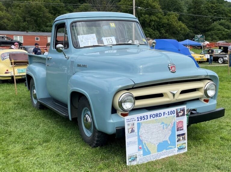 A blue 1953 Ford F-100 truck in a field at a car show with a map of the truck's travels as part of the classic car provenance