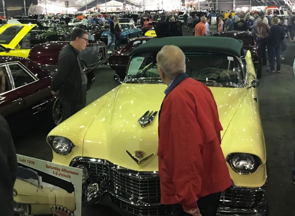2 classic car experts inspecting a yellow Cadillac convertible at a car auction