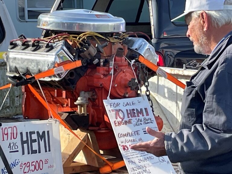 A classic car expert inspecting an orange painted1970 Plymouth Hemi engine at a car show