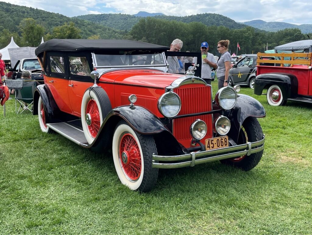 A vintage red and black pre-war 4 door convertible sedan at a car show with 3 people discussing the car and classic car terms