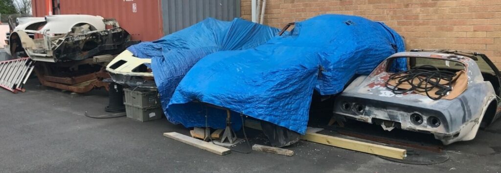 Various Chevy Corvette bodies under blue tarps that were left unrepaired with people not cutting their car restoration losses