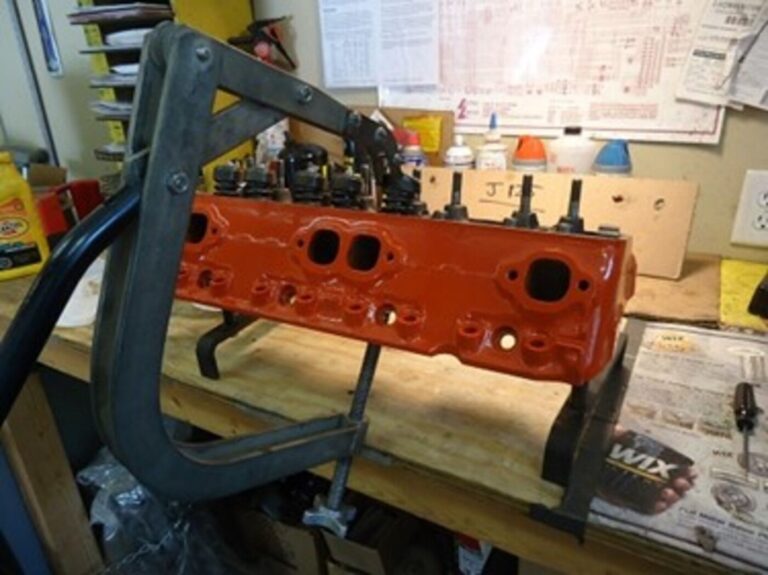 An orange Chevy engine head on a work bench with valve spring installing tool mounted to it avoiding engine rebuilding mistakes