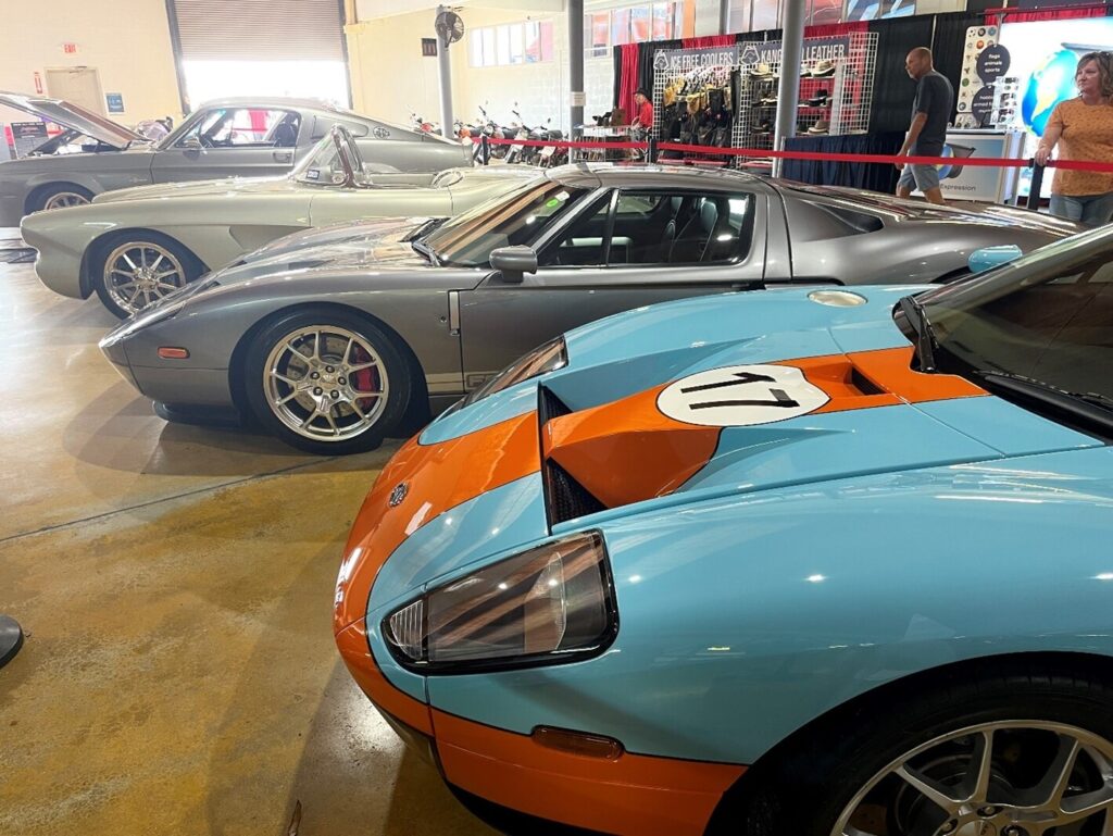 A light blue and silver Ford F40s in front of a white Corvette and silver Ford Mustang on display before buying at a classic car auction