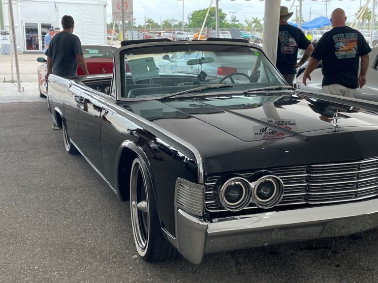 A black 60s 4 door convertible Lincoln on display with 3 men looking around before buying at a classic car auction