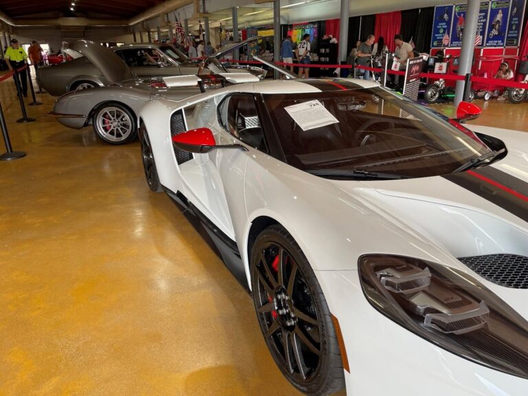 A white with black and red stripes modern Ford GT40 sitting on display in front of a silver Corvette and Ford Mustang before buying at a classic car auction