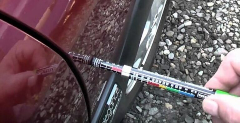 Using a paint gauge on the side of a burgundy car as part of a car pre-purchase inspection