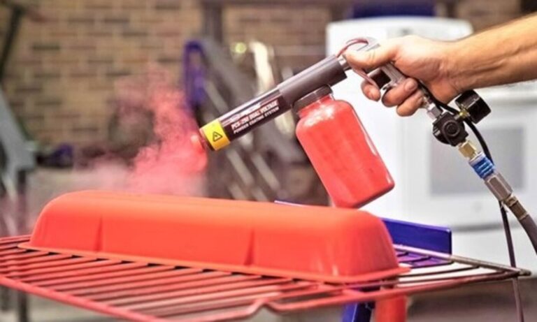 A painter applying red powder coating material onto an engine valve cover as part of the paint process
