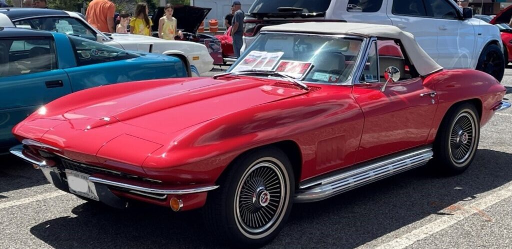 A red 1964 Chevy Corvette with a shite convertible top in a parking lot with a for sale sign on the front window; before buying review tips to avoid classic car fraud
