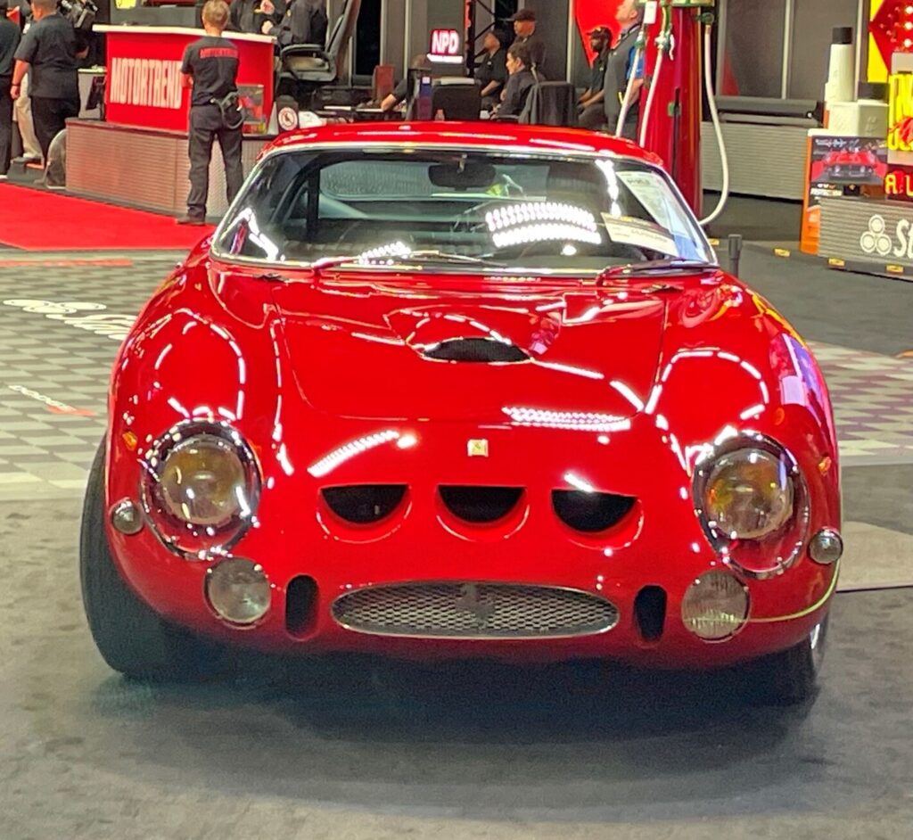 A red Ferrari passing the auction block after being inspected for a car paint job quality by potential buyers