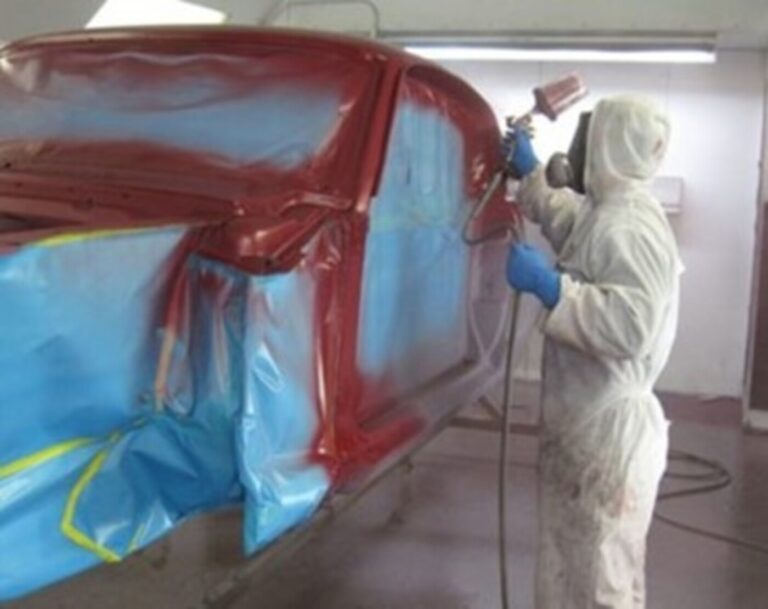 A painter spraying red paint into the jambs of a car as part of the restoration process. inspection car paint job quality is key.