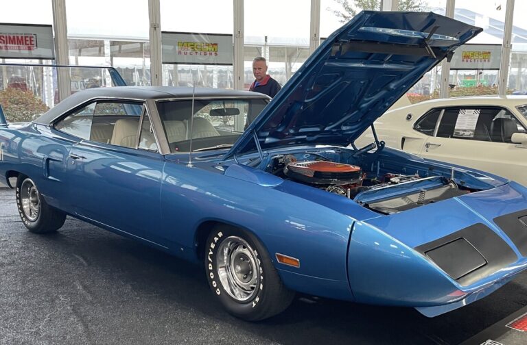A blue Plymouth Superbird parked in front of a white Ford Mustang at a classic cars auctuon