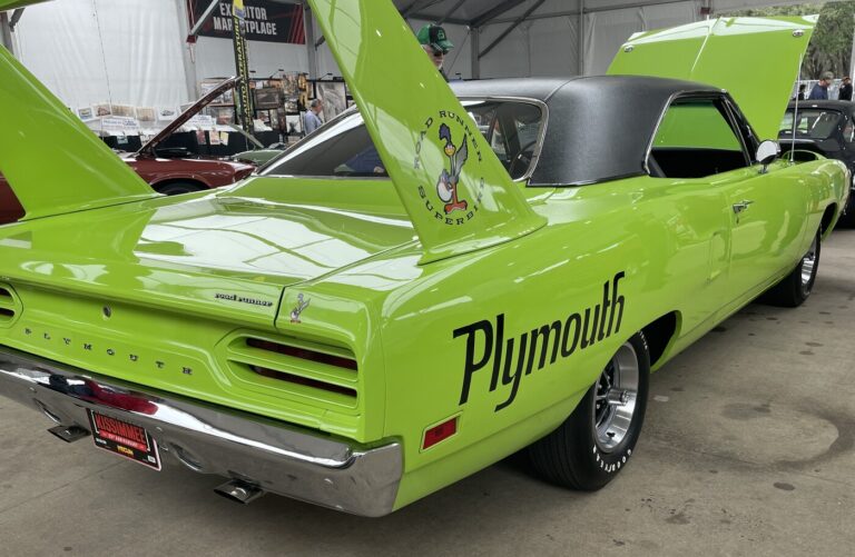 A green Plymouth Superbird parked in a row of classic cars at auction