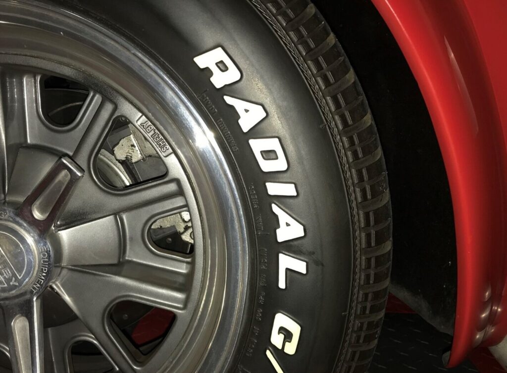 An aluminum wheel with a radial tire with white letters installed with a wheel spacer on a red car