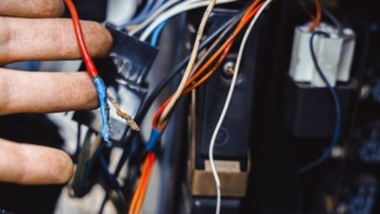 A mechanic holding up a damaged power wire showing the need for replacing wiring